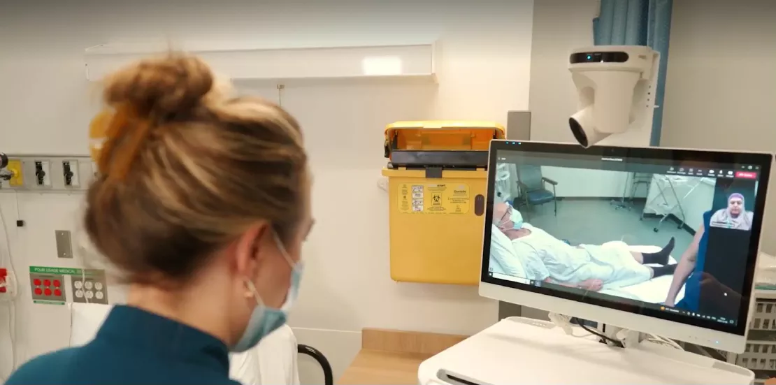 Infirmière au chevet d’un patient communiquant avec une collègue par vidéo