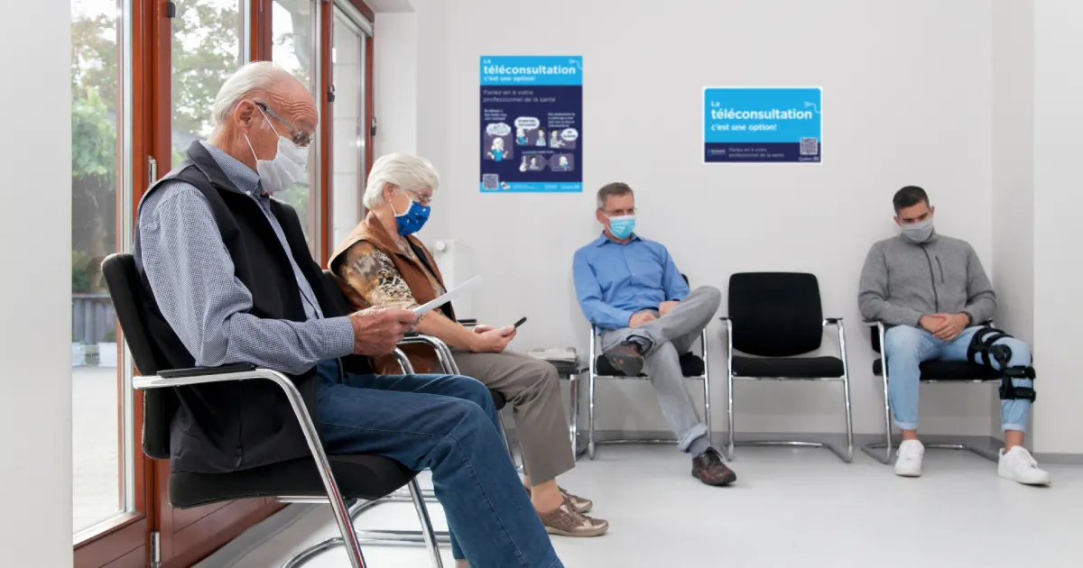 Salle d’attente d’une clinique où on voit des usagers et les affiches de la campagne La téléconsultation, c’est une option! au mur.
